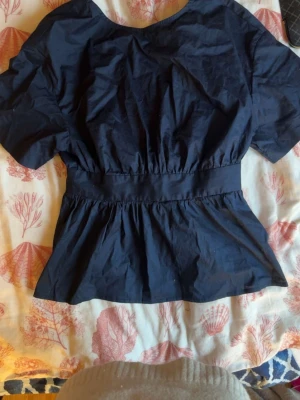 Mörkblå blus med knyt i midjan - Snygg mörkblå blus med korta ärmar och bred midja som knyts i ryggen. Blusen har en lätt v-ringad hals och ett flowy fall nedtill. Perfekt att styla med jeans eller kjol för en trendig look. Slutsåld💕