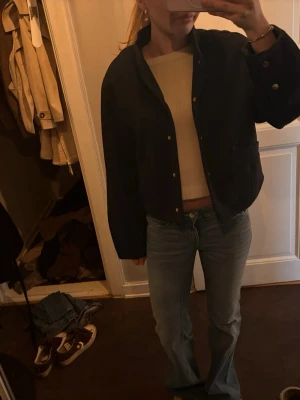 Mörkgrå kort jacka från Zara  med guldknappar - Stilren mörkgrå jacka i kort modell med raka ärmar och snygga guldknappar framtill. Jackan har en klassisk krage och två fickor på sidorna. Perfekt för dig som vill ha en enkel men trendig look. Från Zara