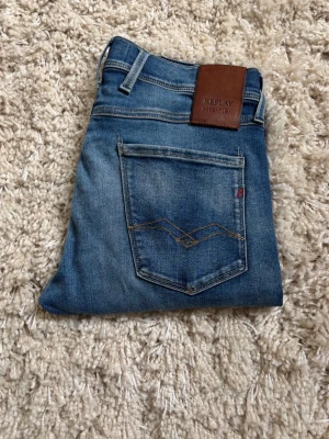 Blå Replay Anbass Hyperflex jeans - Snygga blå jeans från Replay Hyperflex med klassisk femficksmodell och stretchigt material. Jeansen har en skinnpatch med logga bak och coola slitningar framtill för en avslappnad look. Perfekta för dig som gillar en smal passform och bekväma jeans.
