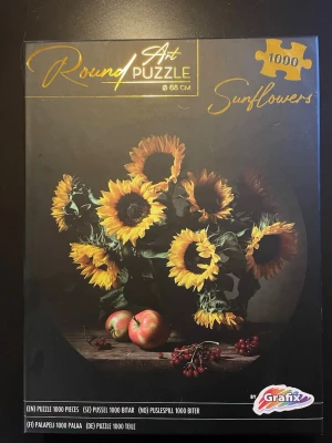 Runt pussel Sunflowers 1000 bitar - Säljer ett runt pussel med motiv av solrosor, äpplen och bär på ett mörkt underlag. Pusslet har 1000 bitar och mäter 68 cm i diameter. Perfekt för dig som gillar konstnärliga motiv och utmanande pussel.