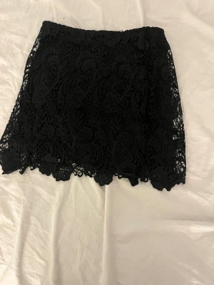 Svart spetskjol från Divided - Säljer en svart kortkjol från Divided med vacker spets och blommigt mönster. Kjolen har en rak passform och är fodrad på insidan för extra komfort. Perfekt att styla med en enkel topp eller stickad tröja.