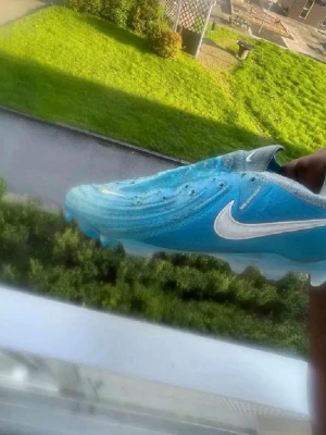 Nike Mercurial och Phantom fotbollsskor - Säljer två par Nike fotbollsskor: ett par Mercurial i blått med vit swoosh och ett par Phantom i beige med svart och guld detaljer. Båda har snörning och är designade för bra grepp på planen. Perfekta för dig som vill ha stilrena och funktionella skor till matchen.