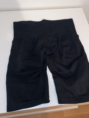 Svarta tajta gymshorts - Säljer ett par svarta shaping shorts med hög midja som formar ens kropp väldigt fint. De är knälånga och perfekt för dig som vill ha stretchiga, bekväma och sköna gymshorts!