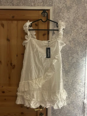 Vit volangklänning med spetsdetaljer - Vit klänning med volanger och spetsdetaljer från boohoo. Helt oanvänd prislappen kvar. Hör av vid frågor!💗