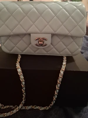 Ljusblå handväska - Supersnygg ljusblå handväska . Kedjerem med insytt läder ger en lyxig känsla och väskan har en tidlös, boxig form. Perfekt för dig som vill ha något exklusivt och trendigt.