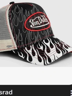 Von Dutch truckerkeps med flames - Säljer en svart och vit truckerkeps från Von Dutch med grymt flames-mönster och röd broderad logga framtill. Kepsen har mesh på sidorna och justerbar snapback. Perfekt för dig som gillar streetwear och vill sticka ut.