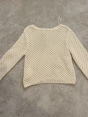 Beige virkad stickad tröja - Säljer en beige stickad tröja med virkat hålmönster och långa ärmar. Tröjan har en avslappnad passform och rund halsringning. Perfekt för lager på lager och ger en trendig look till din outfit. Tröjan har ingen lapp men den är ifrån H&M och är i storlek 146/152❤️Jag har aldrig använt den och den har bara legat i min garderob i ca ett år😅