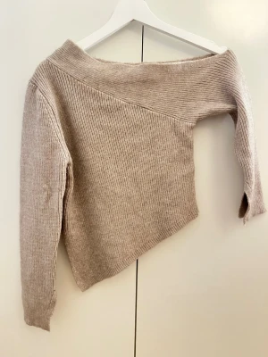 Beige off shoulder stickad tröja SHEIN - Trendig beige stickad tröja från SHEIN med off shoulder-design och ribbad struktur. Tröjan har lång ärm och är gjord i mjukt, stretchigt material som sitter snyggt. Perfekt för dig som gillar en avslappnad men ändå stilren look.
