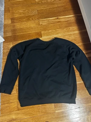 Svart sweatshirt med rund hals - En enkel svart sweatshirt med rund hals och långa ärmar. Tröjan har ribbade muddar vid ärmslut och nederkant. Perfekt för en avslappnad och stilren look.