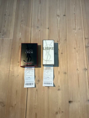 Yves Saint Laurent reseller bundle - Två parfymer från Yves Saint Laurent: Black Opium i svart och kopparfärgad förpackning samt Libre i vit och guld förpackning. Båda har elegant designade kartonger med tydliga logotyper och exklusiv känsla.
