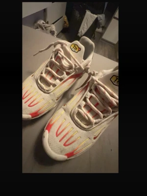 Nike Air Max Plus vita/röda sneakers - Nike Air Max Plus sneakers i vitt mesh med röda och gula detaljer samt svarta och röda inslag på hälen. Klassisk TN-logga på plösen och synlig Air Max-dämpning i sulan. Snygg design med futuristiska linjer och robust yttersula. Perfekta för dig som gillar streetwear.    Priset kan vi sänka