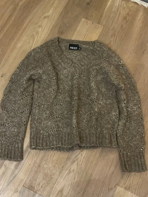 Brun stickad tröja från Pieces - Mysig brun stickad tröja från Pieces med snyggt hålmönster och ribbade muddar vid ärmslut och nederkant. Perfekt för lager-på-lager och har en avslappnad passform med rund hals.