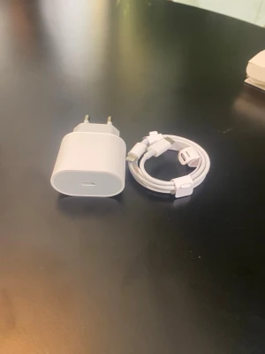 USB C laddare och adapter  - Säljer en vit USB-C väggadapter och en matchande USB-C till Lightning-kabel från Apple. Perfekt för att ladda din iPhone eller iPad snabbt och smidigt. Båda delarna är i klassisk Apple-design med rundade former och tåligt plastmaterial.