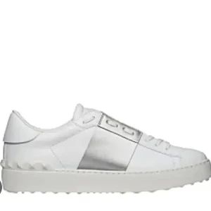 Valentino Garavani vita sneakers - Snygga vita sneakers från Valentino Garavani med en bred silverfärgad panel på sidan och coola nitar längs sulan. Skorna har snörning och är tillverkade i skinn med platt sula och rund tå. Har defekter men sparsamt använda. Perfekta för dig som gillar stilrena och lyxiga detaljer.