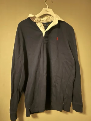 Ralph Lauren tröja mörkblå M – klassisk modell - Mörkblå långärmad tröja från Ralph Lauren med vit krage och röd broderad logo.  Storlek: M Skick: mycket bra  Klassisk och stilren modell som funkar både till vardag och mer uppklätt.  Kan skickas eller hämtas i Göteborg 