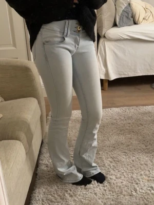 Ljusblå bootcut jeans - Säljer ett par ljusblå bootcut jeans med hög midja och klassiska fem fickor. Jeansen har en snygg passform som framhäver benen och stängs med dragkedja och knapp. Perfekta för en trendig och avslappnad stil. (Framfickorna är utklippta då de syntes igenom jeansen, men ingenting man ser eller märker av)