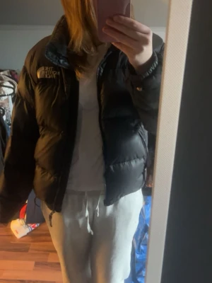 Svart pufferjacka från The North Face - Säljer en svart pufferjacka från The North Face med hög krage och dragkedja framtill. Jackan har en boxig passform och logga på bröstet. Perfekt för kalla vinterdagar och riktigt trendig stil.