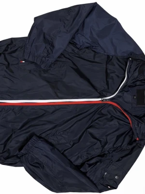 Marinblå vindjacka Tommy Hilfiger - Snygg marinblå vindjacka från Tommy Hilfiger med dragkedja i vitt och rött, samt små logodetaljer på bröstet och ryggen. Jackan har elastiska muddar vid ärmarna och lätt glansigt material som skyddar mot vind. Perfekt för en sportig och stilren look.