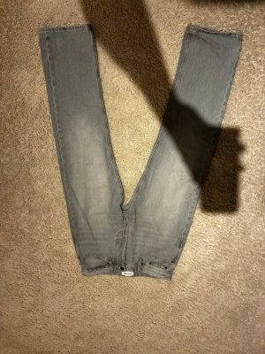 Grå raka jeans från Jack & Jones - Säljer ett par grå jeans från Weekday med rak passform och klassisk femficksdesign. Jeansen har en ljusgrå tvätt och är tillverkade i denim. Perfekta för en avslappnad och trendig stil.