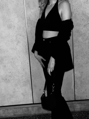 Svart halterneck croppad topp - Säljer en svart croppad halterneck topp med v-ringning och knyt i nacken. Toppens stil är enkel och trendig, perfekt för att skapa en cool look. Materialet känns mjukt och lätt, och den är ärmlös med öppen rygg.