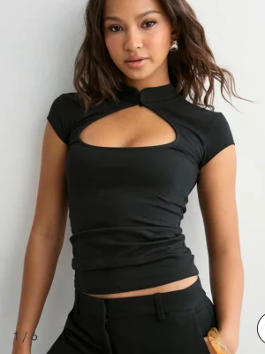 Svart topp med cut out-detalj - Svart topp från Nelly med korta ärmar och snygg cut out-detalj över bröstet!❤️