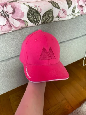 Rosa keps från Mellanstadiet - Snygg rosa keps från mellanskog.se med broderad logga framtill och justerbart spänne bak. Kepsen har böjd skärm och vit kantdetalj. Perfekt för dig som vill sticka ut med färg och enkel stil.