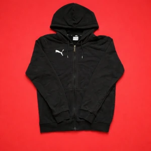 Puma Zip Hoodie - Svart Puma zip hoodie med vit logga på bröstet. Puma står även på dragkedjan och på ändarna av snörena. Bekväm och stilren hoodie som passar till vardag eller träning. Storlek: S