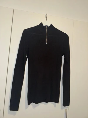 Svart ribbstickad tröja med halvzip - Säljer en svart ribbstickad tröja från Selected Homme med halvzip och hög krage. Tröjan har lång ärm och är tillverkad i ett mjukt, stretchigt material som sitter snyggt på kroppen. Perfekt för lager på lager och enkel att matcha.