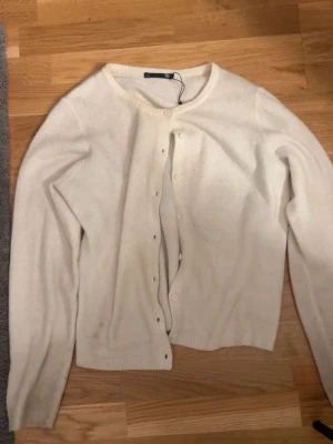 Vit kofta med rund hals - Klassisk vit kofta med rund halsringning och knappar framtill. Långärmad modell i mjukt material, perfekt att slänga över en topp eller t-shirt. Enkel och stilren design som passar till det mesta.