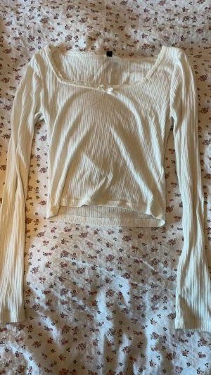 Vit ribbad långärmad tröja med spets - Supersöt vit ribbad topp med långa ärmar, spetskant och liten rosett vid halsringningen. Perfekt att styla med jeans eller kjol för en romantisk vibe💞! Den är rätt så genomskinlig så var beredd på att ha något över om du inte gillar genomskinliga tröjor!🥹ྀིྀི 🤍