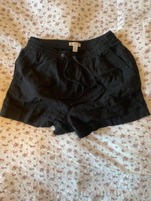Svarta linneshorts med snörning - Säljer ett par svarta shorts från H&M i linne med elastisk midja och snörning framtill. Shortsen har fickor på sidorna och låtsats fickor bak! De är perfekt för varma dagar. Enkel och avslappnad stil som passar till det mesta! 🤗🖤