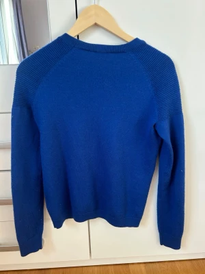 Blå stickad tröja - Snygg blå stickad tröja med rund halsringning och ribbade detaljer på axlar och ärmslut. Tröjan har en enkel, stilren design och är perfekt för lager på lager. Långärmad och i mjukt material.