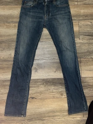 Blå raka jeans från Armani - Säljer ett par klassiska blå jeans från Armani med raka ben och diskret slitning. Jeansen har fem fickor och logga på ena bakfickan. Perfekta till en avslappnad stil och tillverkade i slitstark denim. Skinny jeans 