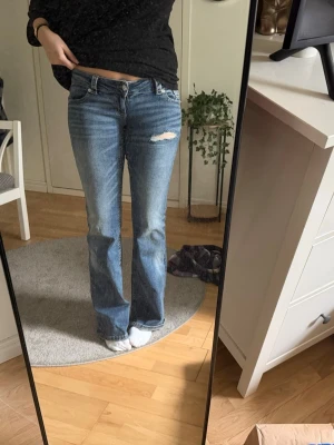 Blå lågmidjade bootcut jeans - Säljer ett par blå jättelågmidjade bootcut jeans från Ginatricots 14+ med slitning och hål på ena låret. Dessutom lite design på bakfickorna! Använda en gång! 