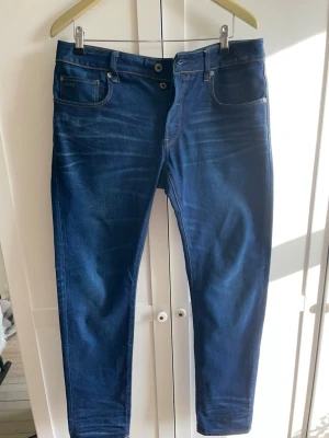 G-star raw jeans - Snygga mörkblå jeans från g-star RAW med klassisk femficksdesign och kontrastsömmar. Jeansen har en slim fit-modell. Midja 32 längd 33