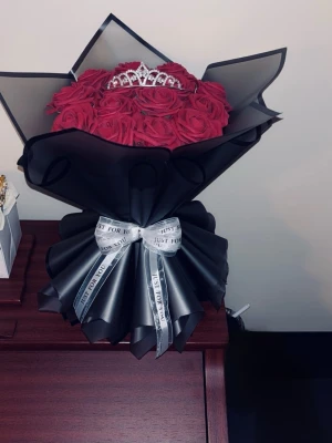 Evighetsrosor röda med tiara - Snygg bukett med Evighetsrosor inslagna i svart papper och dekorerad med en glittrig tiara på toppen. Buketten är knuten med ett vitt band med texten 'Just for you'. Perfekt som present eller dekoration.