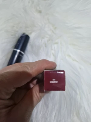 MAC Dubonnet 108 Läppstift - MAC Dubonnet 108 är ett klassiskt läppstift i en djup rödbrun nyans. Hylsan är svart med silverdetaljer och har den ikoniska MAC-loggan. Läppstiftet har en krämig formula som ger en snygg och intensiv färg till läpparna.