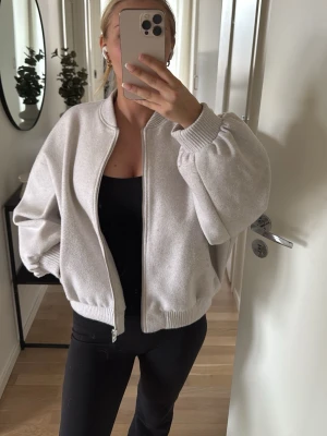 Bomberjacka Zara - Säljer en ljusbeige/vit bomberjacka i oversized modell med breda ärmar och ribbade muddar vid ärmslut och nederkant. Jackan har dragkedja framtill och en mjuk, borstad yta som ger en chill och trendig look. Perfekt för dig som gillar en avslappnad stil. En liten fläck på armen som syns på sista bilder. Knappt använd.