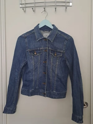 Blå jeansjacka - Jeansjacka från äldre hm i klassisk modell med knappar framtill och två bröstfickor med lock. Jackan har en figurnära passform, skjortkrage och kontrastsömmar. Hittar inga defekter. Str. 38 🩷