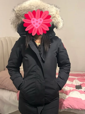 Mörk blå/svart victoria parka från Canada Goose - Snygg svart parkas från Canada Goose med klassisk patch på ärmen och stor huva med fluffig fuskpäls. Jackan har dragkedja och knappar framtill samt två fickor. Perfekt för kalla dagar när du vill hålla dig varm och stilren. Den är äkta, köptes 3 år sen, använt den 6 gånger max. Och är nästan helt ny och fräsch. Passar S och xs.