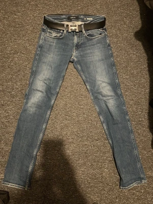 Blå slim fit jeans från Replay - Säljer ett par blå slim fit jeans från Replay med klassisk femficksdesign och snygga slitningar. Jeansen har en något tvättad look och är tillverkade i bomull med stretch för extra komfort. Perfekta för en trendig och avslappnad stil. Bälte ingår ej kan diskuteras vid bra pris