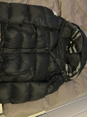 Svart pufferjacka från Burberry - Svart pufferjacka från Burberry som även går att göra om till väst. Köpt denna vintern och använd drygt 4 gånger.