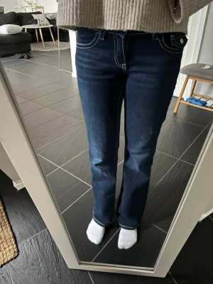 Mörkblå bootcut jeans med kontrastsömmar - Säljer ett par mörkblå bootcut jeans från Gina tricot Young, de har vita sömmar. Jeansen har normal midja och lätt utsvängda ben. Perfekta för dig som gillar en tidlös men ändå trendig look. Sömnen på baksidan har gott upp lite, men går att laga lätt. 