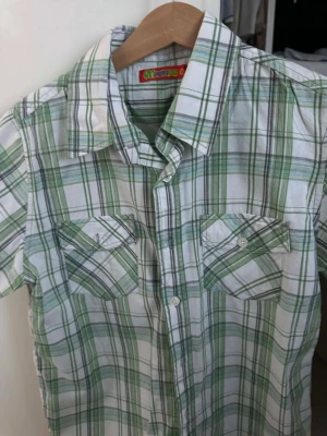 Grönvit rutig skjorta kort ärm - Kortärmad skjorta i vitt och grönt med rutigt mönster. Två bröstfickor med knappar och klassisk krage. Perfekt för en avslappnad stil. Märke: My Wear.