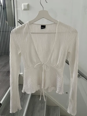 Vit omlottopp med knyt från Ginatricot, XS - Säljer en vit omlottopp från Ginatricot med lång ärm och knyt i midjan. Toppen har ribbad struktur och lätt volang vid nederkanten💖