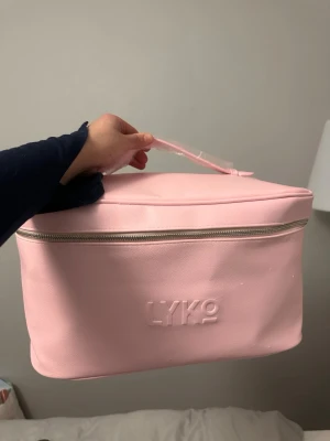 Ljusrosa necessär från Lyko - Säljer en ljusrosa necessär från Lyko i mjukt konstläder. Väskan har en praktisk dragkedja runt om och ett smidigt handtag upptill. Perfekt för att organisera smink eller hudvårdsprodukter. Enkel, stilren design med Lyko-logga på framsidan.