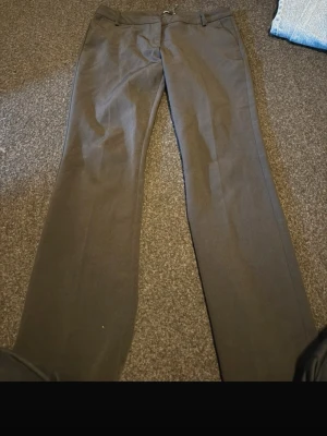 Mörkgrå kostymbyxor med raka ben - Snygga mörkgrå kostymbyxor med raka ben och klassisk passform. Byxorna har hällor för skärp, diskreta fickor fram och stängs med dragkedja och knapp. Perfekta för en clean och stilren look.