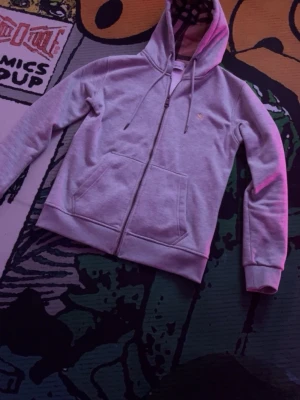 Grå zip hoodie från Burberry - Snygg grå zip hoodie från Burberry med klassisk huva och dragsko. Broderad Burberry-logga på bröstet och fickor framtill. Insidan av huvan har ett rutigt mönster som ger extra stilpoäng. Perfekt för dig som gillar streetwear och premiumkänsla.