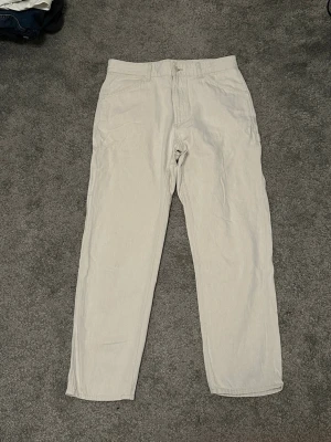 Beige cargobyxor Uniqlo - Säljer ett par stilrena beige cargobyxor med raka ben och hög midja. Byxorna har klassiska cargofickor på sidorna, bälteshällor och stängs med knapp och dragkedja. Perfekta för en avslappnad och trendig look.