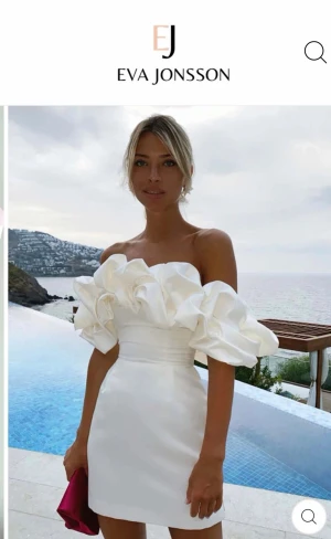 Studentklänning! Off shoulder (Vit)  med volangärm - Trendig off shoulder klänning från Eva Jonsson med stora volangärmar och figurnära passform. Säljer i vitt och men bilden med ljusrosa visade också passformen bra så jag la in den med. satinliknande material som ger en lyxig känsla. Perfekt för dig som vill sticka ut med en statementklänning.